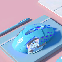 Blue gaming mouse with a brand logo on a pink surface with a pen and notebook.